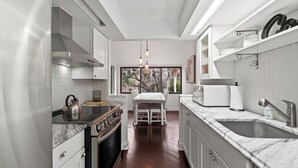 A modern kitchen with a central island, stainless steel appliances, and a view of trees through the window. - Treetops 4904 by Avantstay Hilton Head Condo + Balcony + Shared Pool + Tennis Court + Near Beach and Dining (Hilton Head Island)