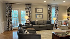 A living room with a sofa, armchairs, a coffee table, and a glass-top table. There are two lamps, a ceiling fan, and a door with glass panels. - Masters Rental: 4BR/3.5 Bath, 4.7 miles to course (Augusta)