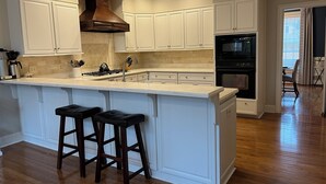 A modern kitchen with white cabinetry, a large island with stools, and built-in appliances. - Masters Rental: 4BR/3.5 Bath, 4.7 miles to course (Augusta)