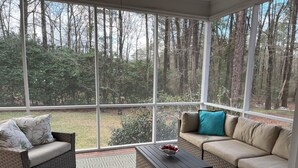 A sunroom with a large glass window, a wicker sofa, a matching armchair, and a wooden coffee table. - Masters Rental: 4BR/3.5 Bath, 4.7 miles to course (Augusta)