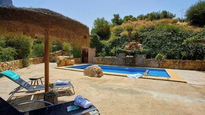 A pool area with lounge chairs, a thatched umbrella, and a stone wall. - Refugio La Sima El Gastor by Ruralidays (Cádiz)