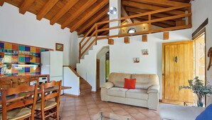 A spacious living area with a wooden staircase, a dining table with chairs, a sofa with a red pillow, and a wooden door. - Refugio La Sima El Gastor by Ruralidays (Cádiz)