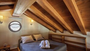 A bedroom with a sloped ceiling, a bed with pillows, a round window, and wall-mounted lights. - Refugio La Sima El Gastor by Ruralidays (Cádiz)