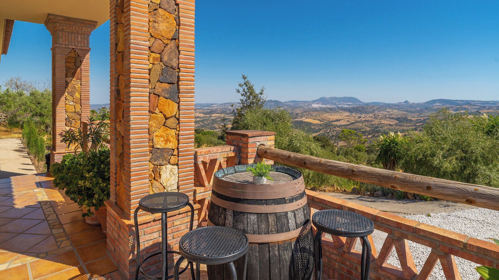 A patio with a stone wall, a wooden barrel, and two round tables.