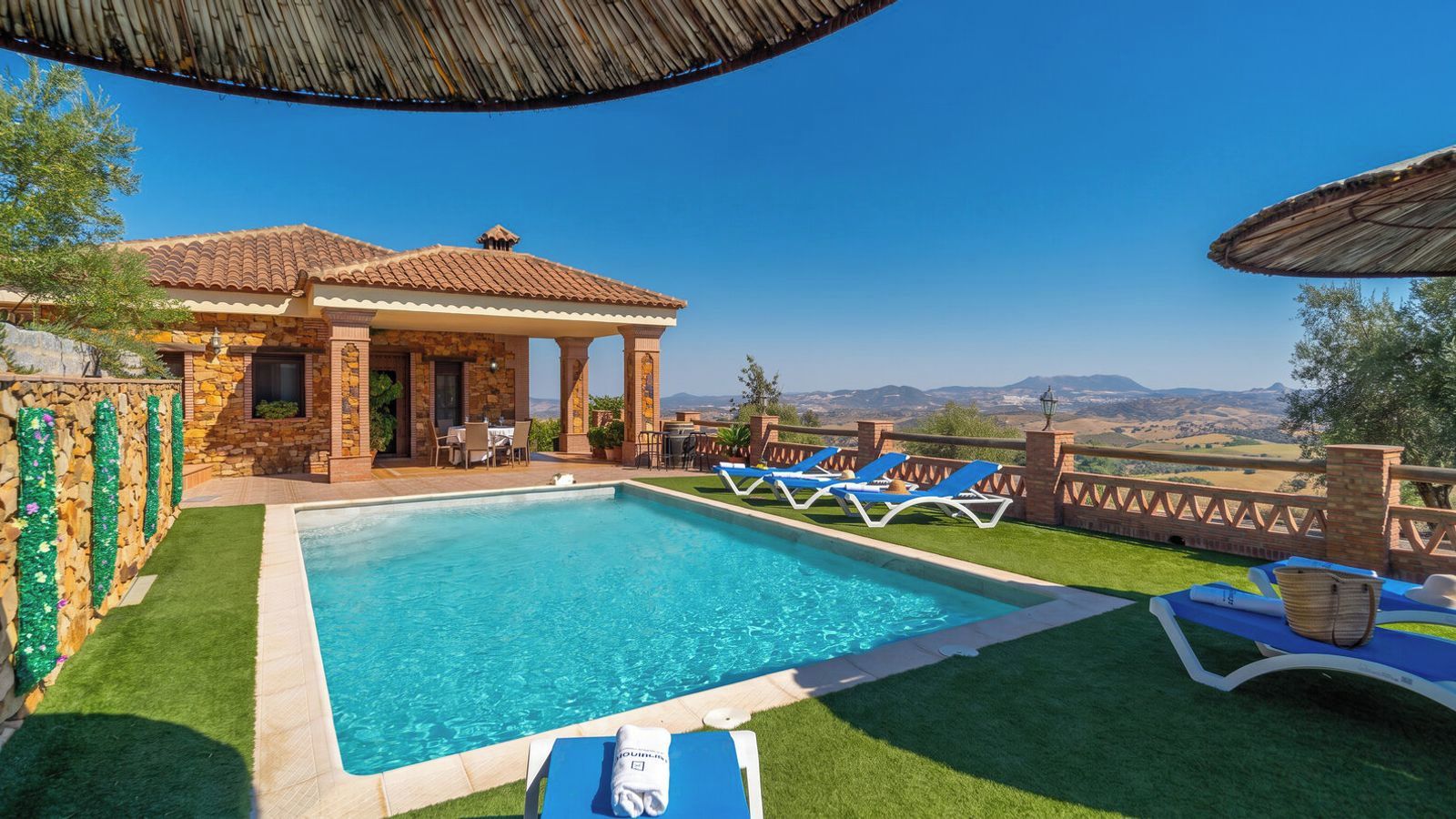 A swimming pool with lounge chairs, a covered seating area, and a view of the landscape.