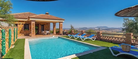 A swimming pool with lounge chairs, a covered seating area, and a view of the landscape.