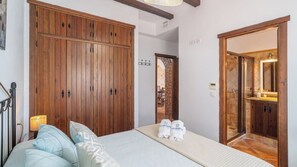 A bedroom with a large wooden wardrobe, a bed with patterned bedding, and a bathroom visible through an open door.