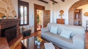 A cozy living room with a fireplace, a sofa with patterned cushions, and a coffee table with plants.