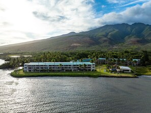 A coastal hotel with multiple buildings, a beachfront, and a mountainous backdrop. - Molokai Oceanview Oasis | Wavecrest C211 (Kaunakakai)