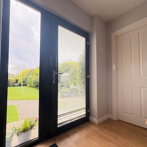 A room with a sliding glass door leading to a garden, a white door, and a wooden floor.