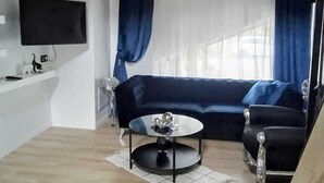 A living room with a wooden ceiling, a black sofa, a round coffee table, and a TV mounted on the wall. - Maison moderne à 20 minutes de Strasbourg (Kurtzenhouse)