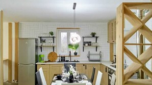 A modern kitchen with white cabinetry, a dining table set for four, and a wooden staircase. - Maison moderne à 20 minutes de Strasbourg (Kurtzenhouse)