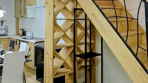 A modern kitchen with white cabinets, a wooden staircase with a geometric design, and a hanging light fixture. - Maison moderne à 20 minutes de Strasbourg (Kurtzenhouse)