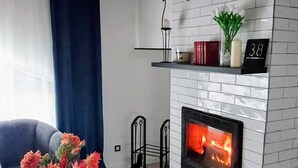 A living room with a fireplace, a sofa, a coffee table with flowers, and a blue curtain. - Maison moderne à 20 minutes de Strasbourg (Kurtzenhouse)