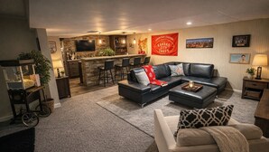 A modern living room with a sectional sofa, a coffee table, and a bar area with stools. - Marvelous 4-bedroom house with Pool in lovely Lenexa World Cup Ready (Lenexa)