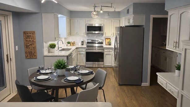 A modern kitchen with white cabinets, stainless steel appliances, and a dining area with a round table set for four. - Marvelous 4-bedroom house with Pool in lovely Lenexa World Cup Ready (Lenexa)