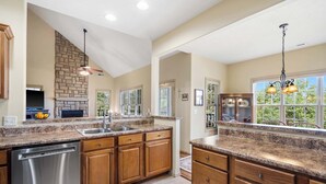 A spacious kitchen with granite countertops, wooden cabinets, a built-in dishwasher, and a stone accent wall. - The Charming Retreat For 6! (Branson West)
