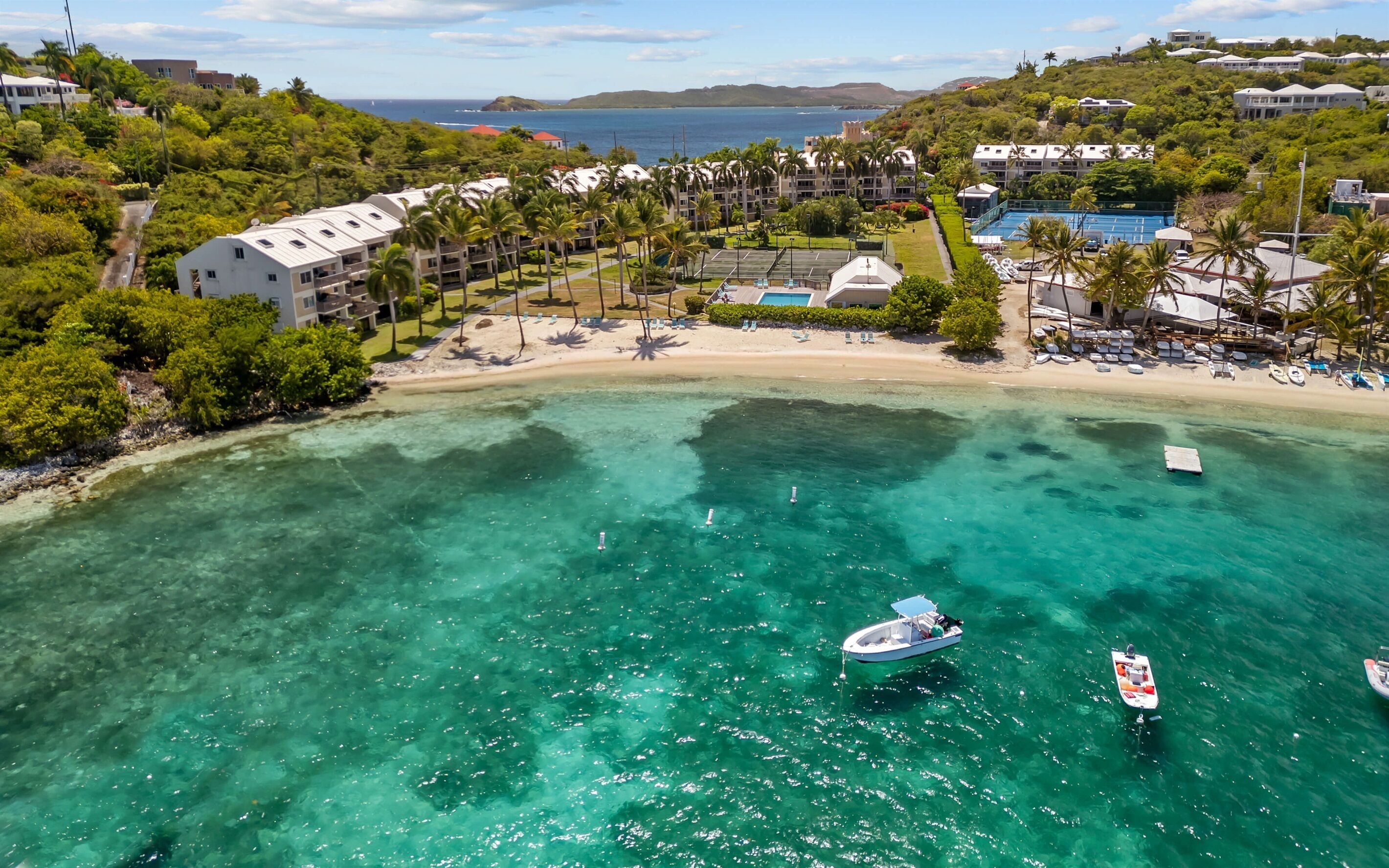 Um resort com praia, águas turquesa cristalinas e um barco.