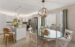 A modern kitchen with white cabinets, a stainless steel refrigerator, a glass dining table, and a hanging chandelier. - Beachfront, Balcony, Pool, Gym, Ocean Views (St. Thomas)