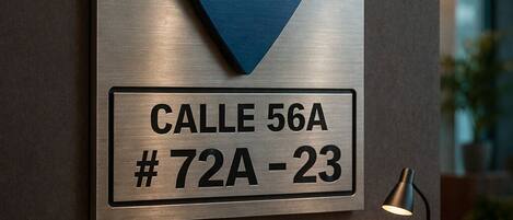 A hotel sign with a blue location marker and a metal plaque indicating the room number.