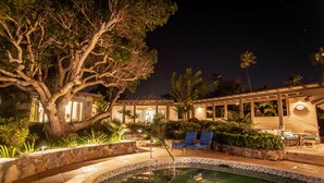 A nighttime pool area with a large tree, lounge chairs, and a building with a covered patio. - Yellowbird Villa, Pool, Ocean Views, 6 bed, Luxury (St. Thomas)