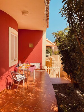 Ein rotes Gebäude mit einer gefliesten Terrasse, einem Tisch mit rot-weiß kariertem Tuch und Stühlen.