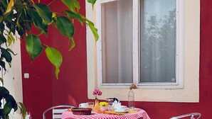 A red-walled room with a window, a table with a checkered tablecloth, two metal chairs, and a potted plant. - Studio for 2. *Free Pickup Stella Maris! (Maio)