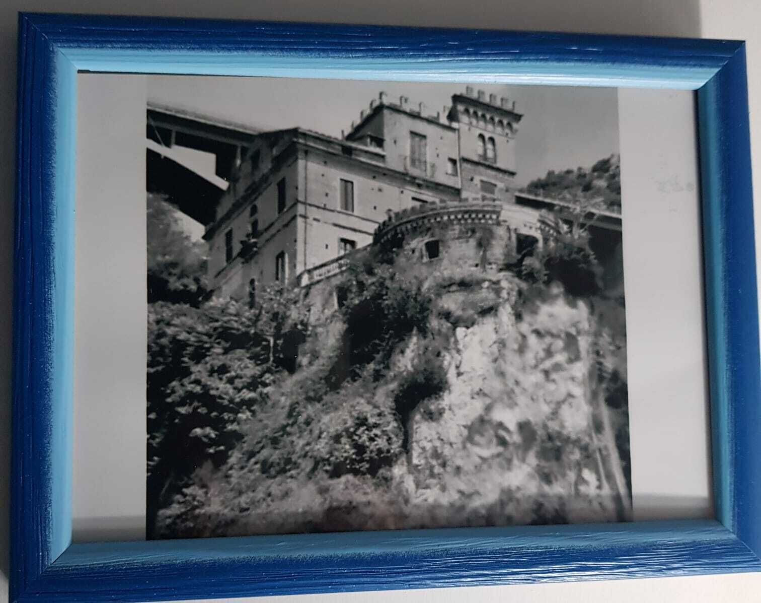 A black and white photograph of a historic building with a tower, situated on a rocky hill.