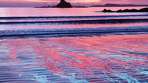 Ein Strand mit Sonnenuntergang, Wellen und in der Ferne Inseln.