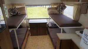 Ein kompaktes Wohnmobil-Interieur mit zwei Schlafbereichen, einer kleinen Küchenzeile und Blick ins Freie.