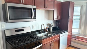 Una cocina moderna con electrodomésticos de acero inoxidable, armarios de madera, encimera de granito y una ventana que proporciona luz natural.