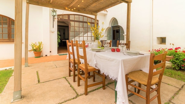 An outdoor patio with a table set for dining, surrounded by wooden chairs and a pergola overhead. - Sardinia Casa di Nonna Ida 7 rooms + garden+BBQ (Villaputzu)