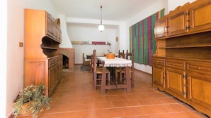 A dining area with a wooden table and chairs, a hanging light fixture, and a brick fireplace. - Sardinia Casa di Nonna Ida 7 rooms + garden+BBQ (Villaputzu)