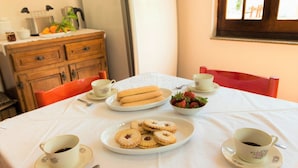 A dining table with a white tablecloth, two cups of coffee, a plate of cookies, and a bowl of strawberries. - Sardinia Casa di Nonna Ida 7 rooms + garden+BBQ (Villaputzu)