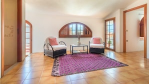 A spacious room with a tiled floor, two wicker chairs, a small table, and a large arched window. - Sardinia Casa di Nonna Ida 7 rooms + garden+BBQ (Villaputzu)