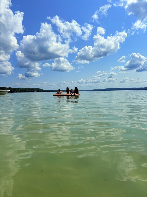 Un grupo de personas en una balsa sobre aguas tranquilas, con cielo despejado y tierra a lo lejos.