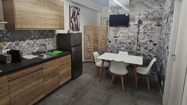 Una cucina moderna con mobili in legno, un frigorifero nero, un tavolo da pranzo con sedie e una TV montata su una parete strutturata.