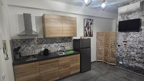 Una cucina moderna con mobili in legno, un frigorifero nero, una parete a mosaico e un televisore a schermo piatto montato su una parete strutturata.