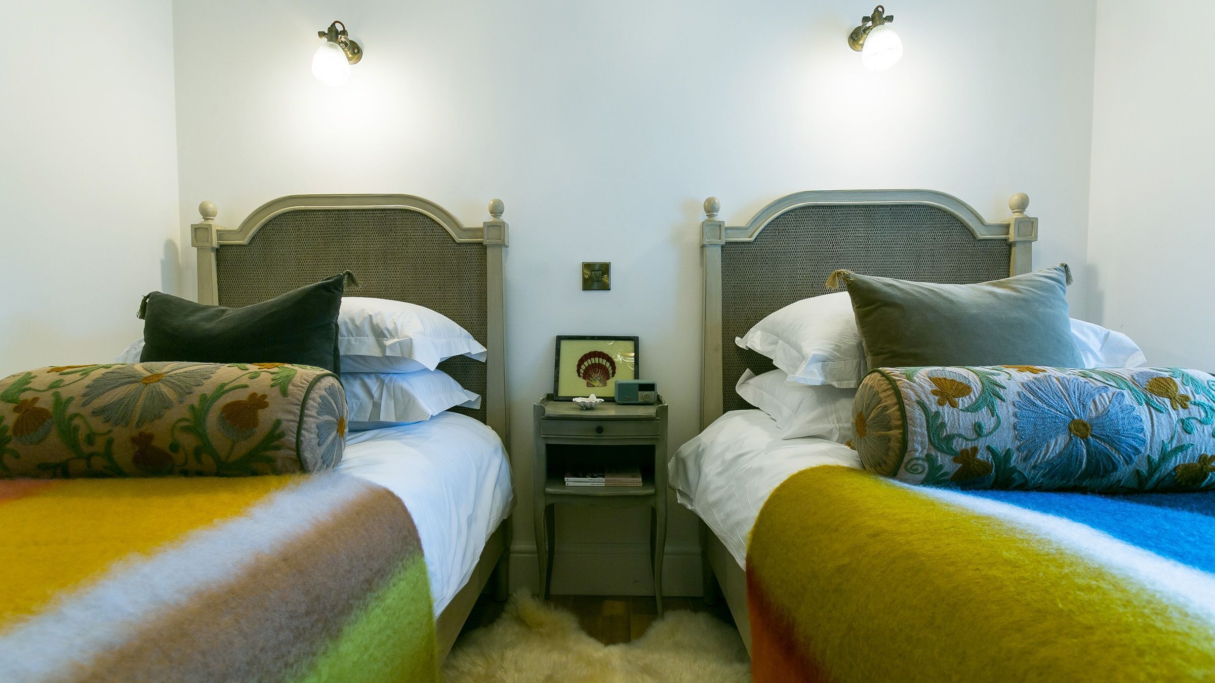 Une chambre double avec deux lits, chacun doté d’une tête de lit, d’une table de chevet avec une radio et d’un luminaire fixé au mur.
