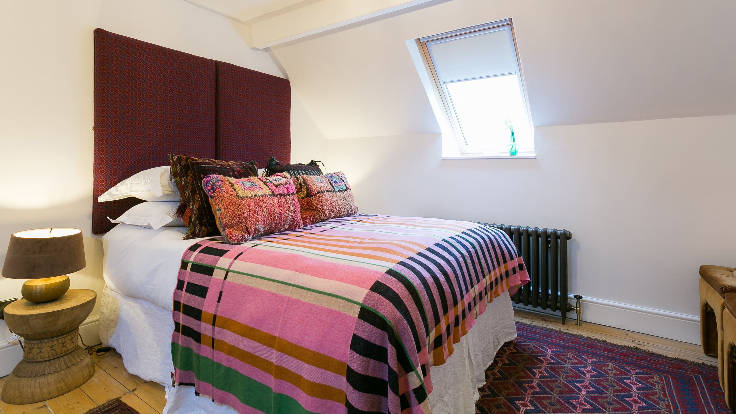 Un dormitorio con una cama grande, una ventana con vistas, un radiador y una lámpara sobre un pedestal de madera.