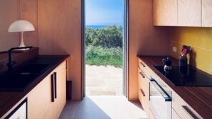 Cuina moderna amb armaris de fusta, taulell negre i vista a vegetació i muntanyes a través d'una porta de vidre.