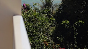 Vista de una playa con agua turquesa cristalina, cielo parcialmente nublado y abundante vegetación.