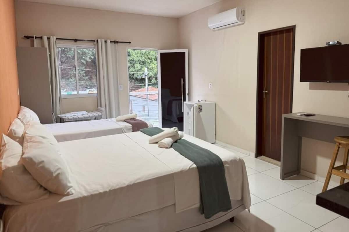 Habitación de hotel con dos camas, un escritorio, una silla, un aire acondicionado y un televisor.