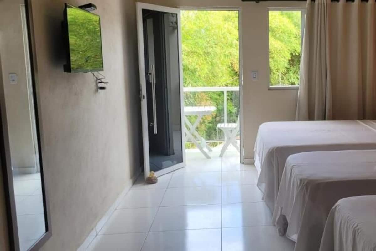 Habitación de hotel con dos camas, un televisor montado en la pared y un balcón con vistas a zonas verdes.