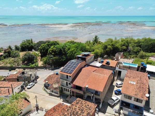 Zona residencial costera con edificios de techos rojos, paneles solares y vistas al mar.