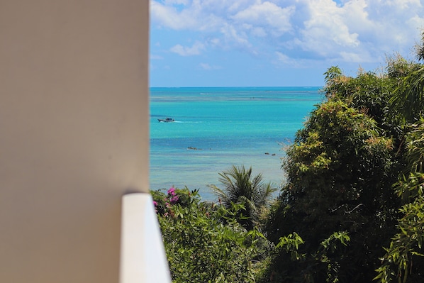 A view of a tropical beach with clear turquoise waters, a boat, and lush greenery.