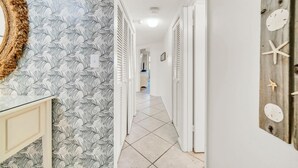 A hallway with a patterned wallpaper, a glass-top table, and a wooden wall decoration. - Jetty East 106b (Destin)