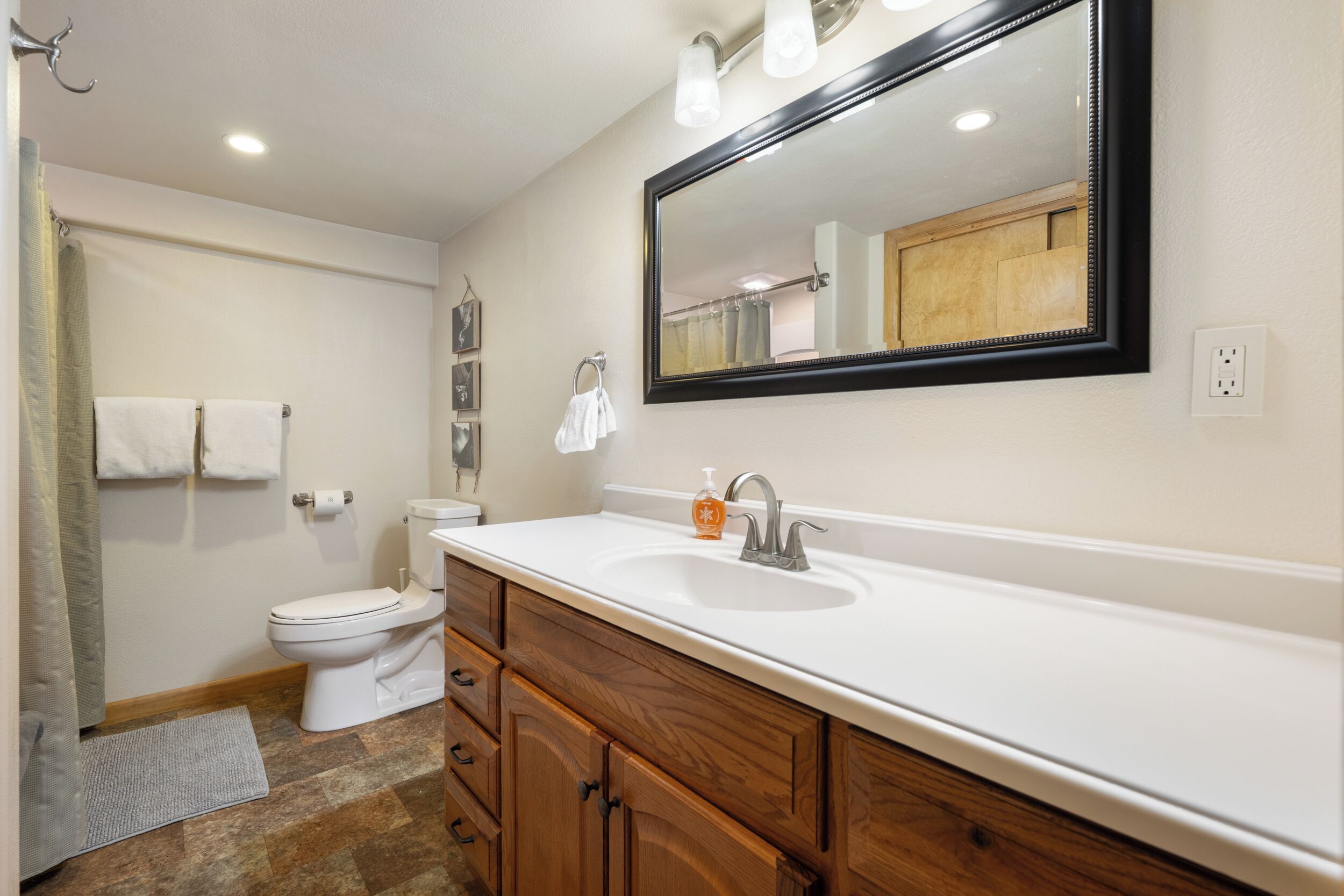 A bathroom with a white sink, wooden vanity, and a large mirror.