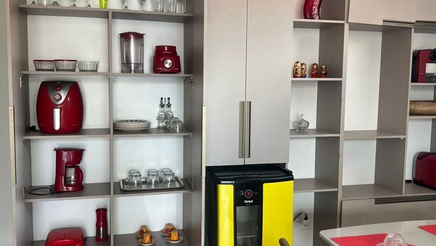 Une cuisine compacte équipée d’un réfrigérateur intégré, d’une machine à café et d’un four à micro-ondes. On y trouve des étagères avec de la verrerie et des ustensiles de cuisine.