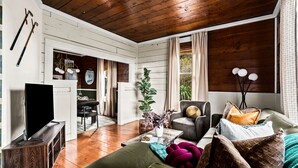 Un salon chaleureux avec un plafond en bois, un téléviseur à écran plat, un canapé confortable et un coin repas comprenant une table et des chaises.